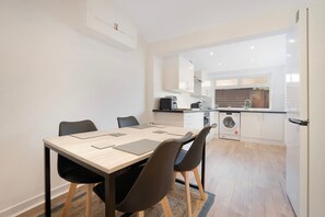 Eine moderne Küche mit Essbereich, inklusive Tisch mit Stühlen, einer Waschmaschine und einem Kühlschrank.