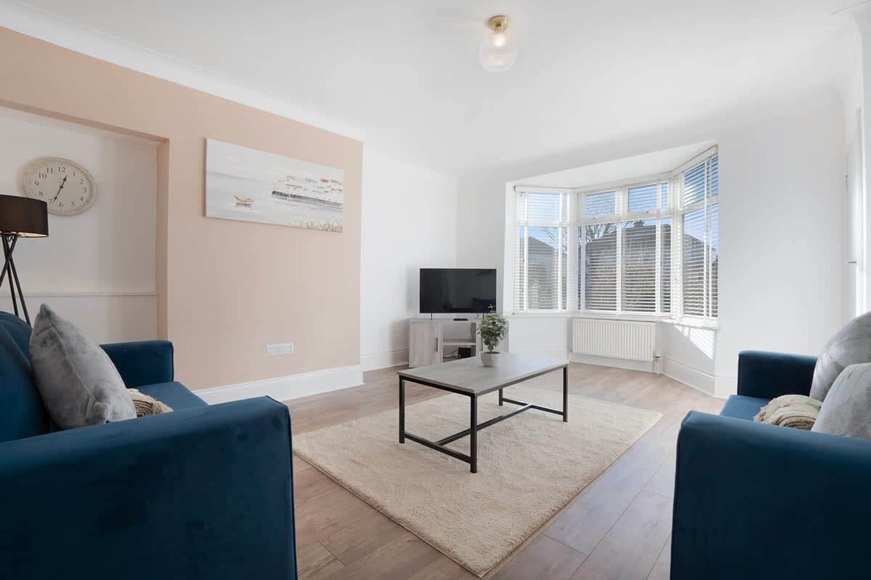 A modern living room with a sofa set, a coffee table, a TV, and a large window with blinds.