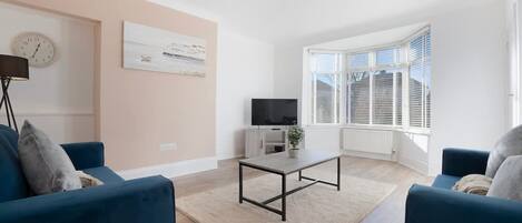 Una sala de estar moderna con un juego de sofá, una mesa de centro, un televisor y un ventanal con persianas.