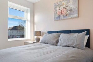 A bedroom with a bed, a nightstand, a lamp, and a window. - New 2BR in 53 Rowlington Terrace (Ashington)