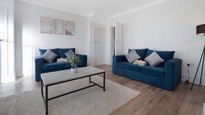 A modern living room with two blue sofas, a coffee table, and a floor lamp. - New 2BR in 53 Rowlington Terrace (Ashington)