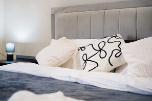 Una cama con ropa de cama blanca y cabecera gris.
