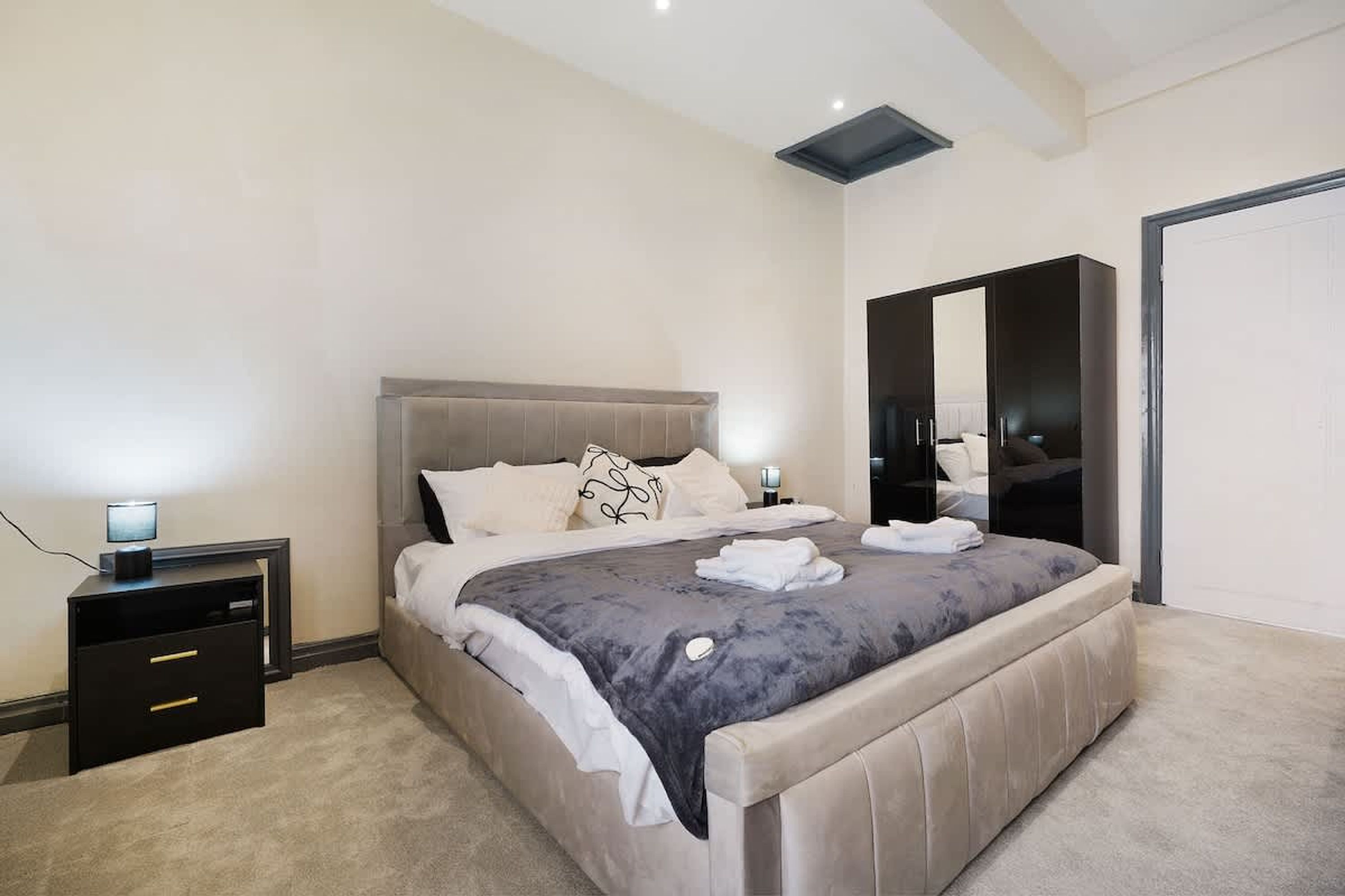 Quarto moderno com uma cama grande, mesas de cabeceira, guarda-roupa e uma luminária no teto.