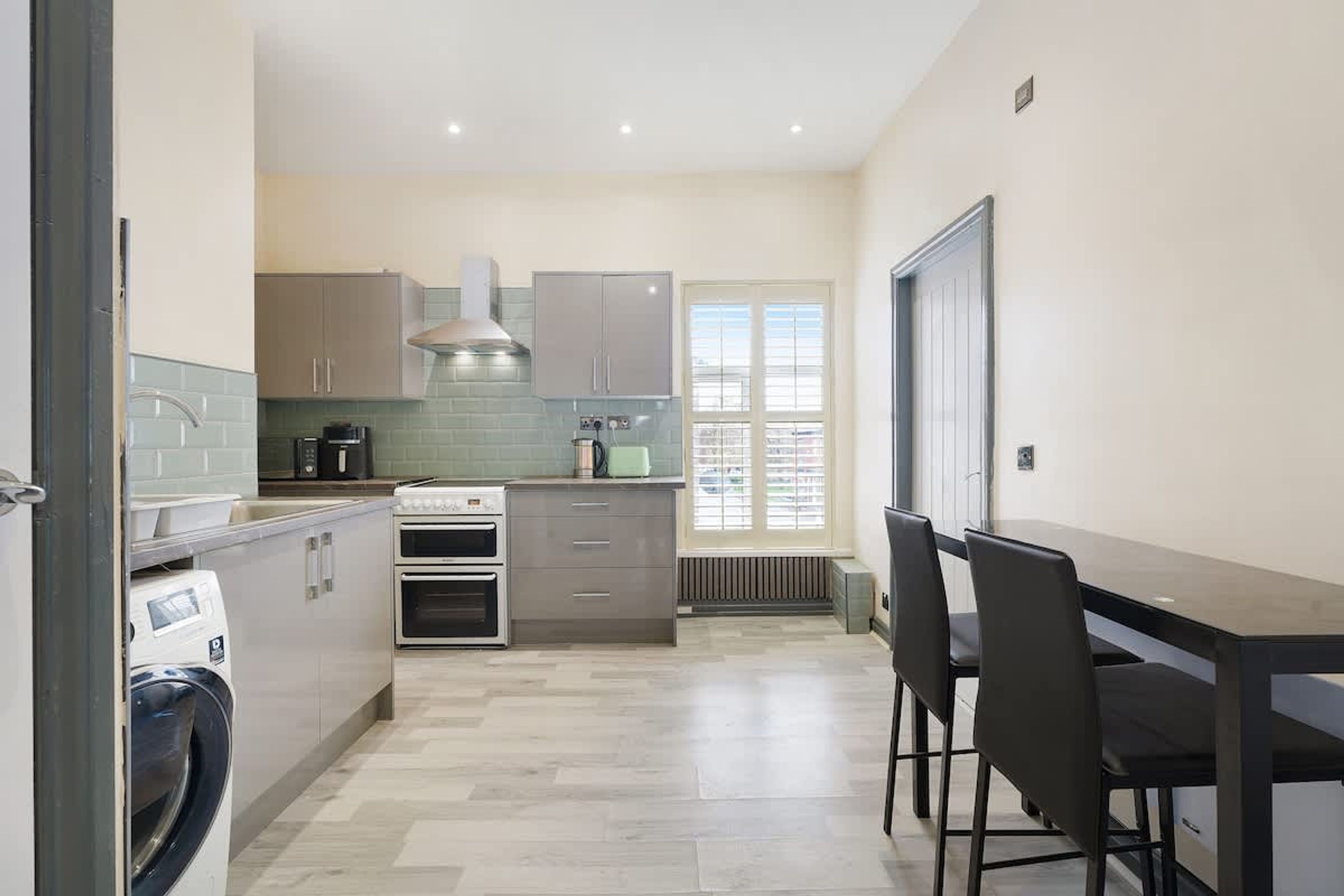 A modern kitchen with a built-in oven, a coffee maker, and a window with blinds.