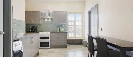 A modern kitchen with a built-in oven, a coffee maker, and a window with blinds.