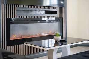 A modern fireplace with a glass front, a small potted plant on the mantel, and a sleek, curved coffee table in front. - Modern City Apartment Sleeps 4 by Stay With Us (Bolton)