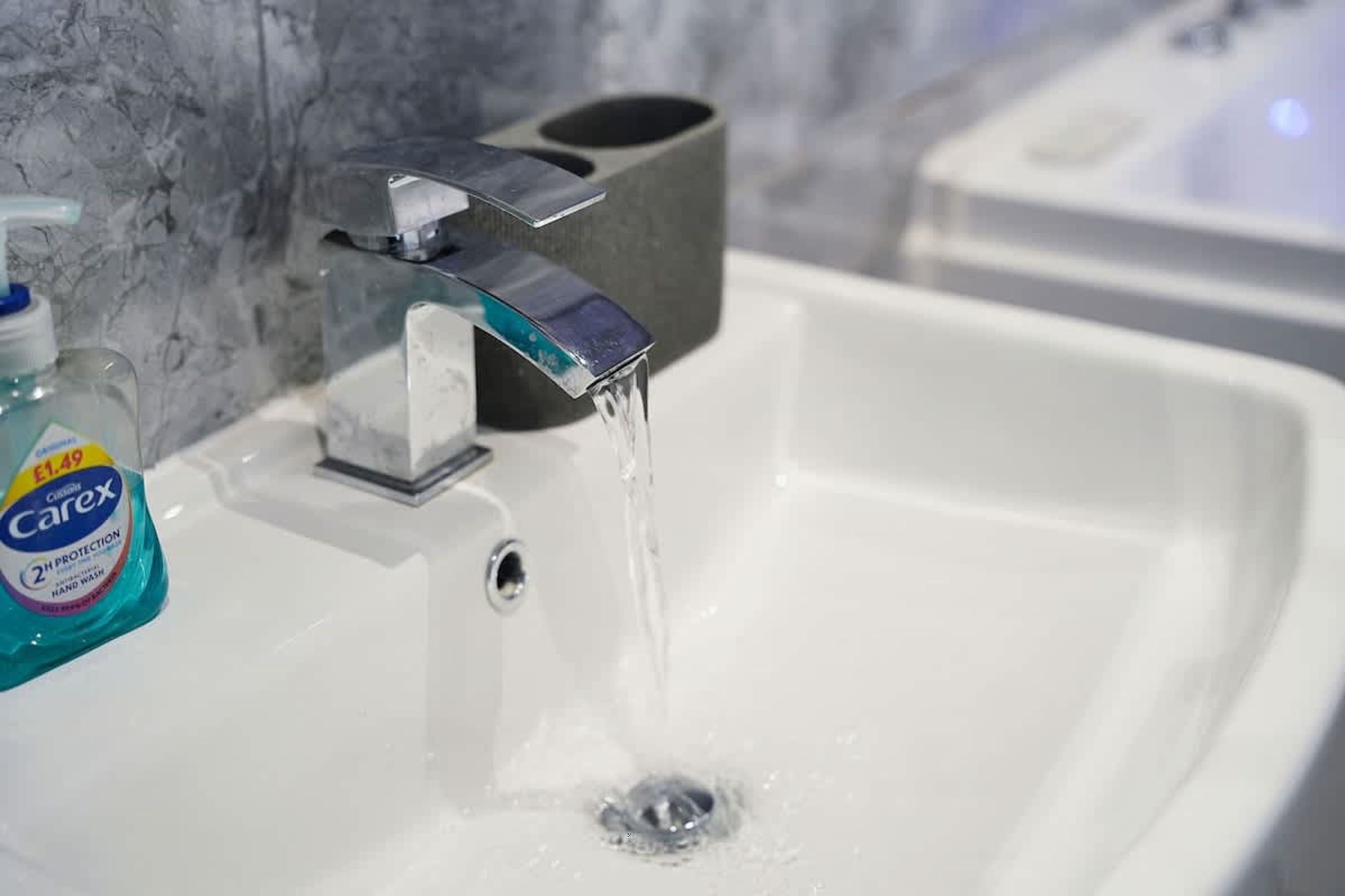 A bathroom sink with a faucet, a soap dispenser, and a bottle of hand soap.