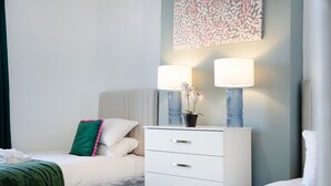 Une chambre d’hôtel avec un lit, une table de chevet dotée de deux lampes, une plante en pot et une œuvre d’art accrochée au mur.