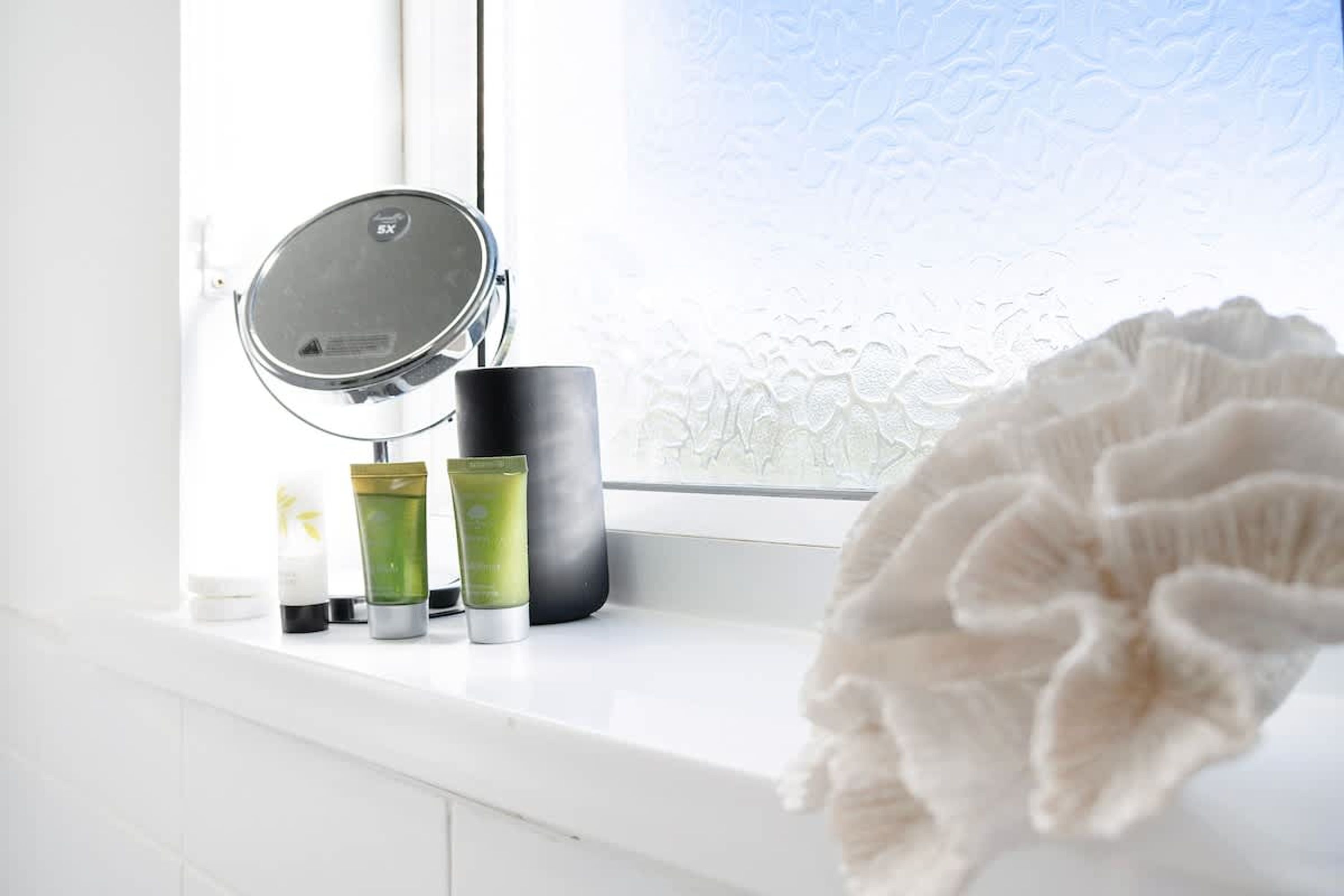 Un tocador de baño con espejo, un altavoz negro y tres frascos de productos para el cuidado de la piel.