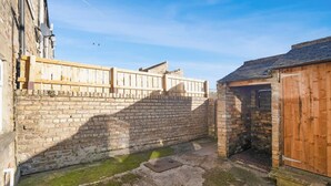 Une cour bordée d’un mur de briques, d’une clôture en bois et d’un petit bâtiment en bois.