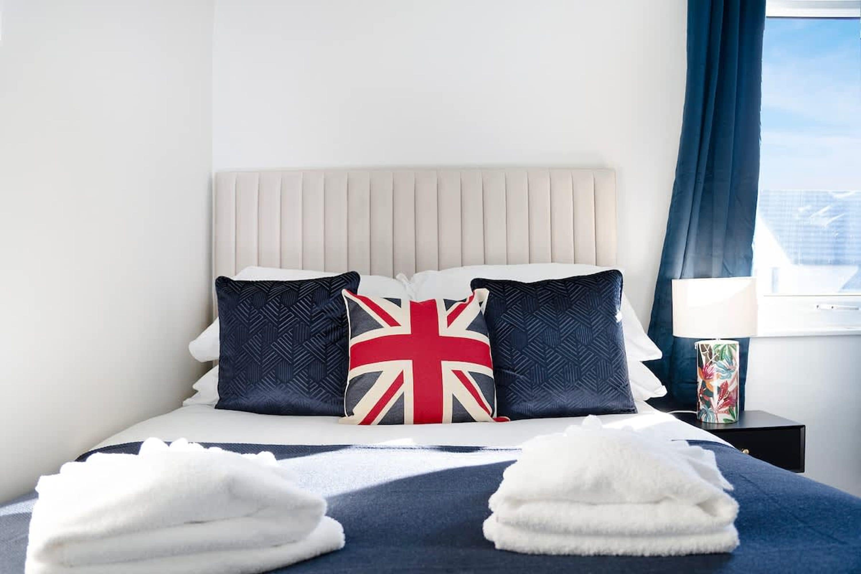 A hotel room with a bed, pillows, a nightstand, a lamp, and a window with curtains.