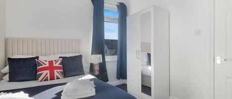 A hotel room with a bed, a wardrobe, a window with curtains, and a view of the sky.