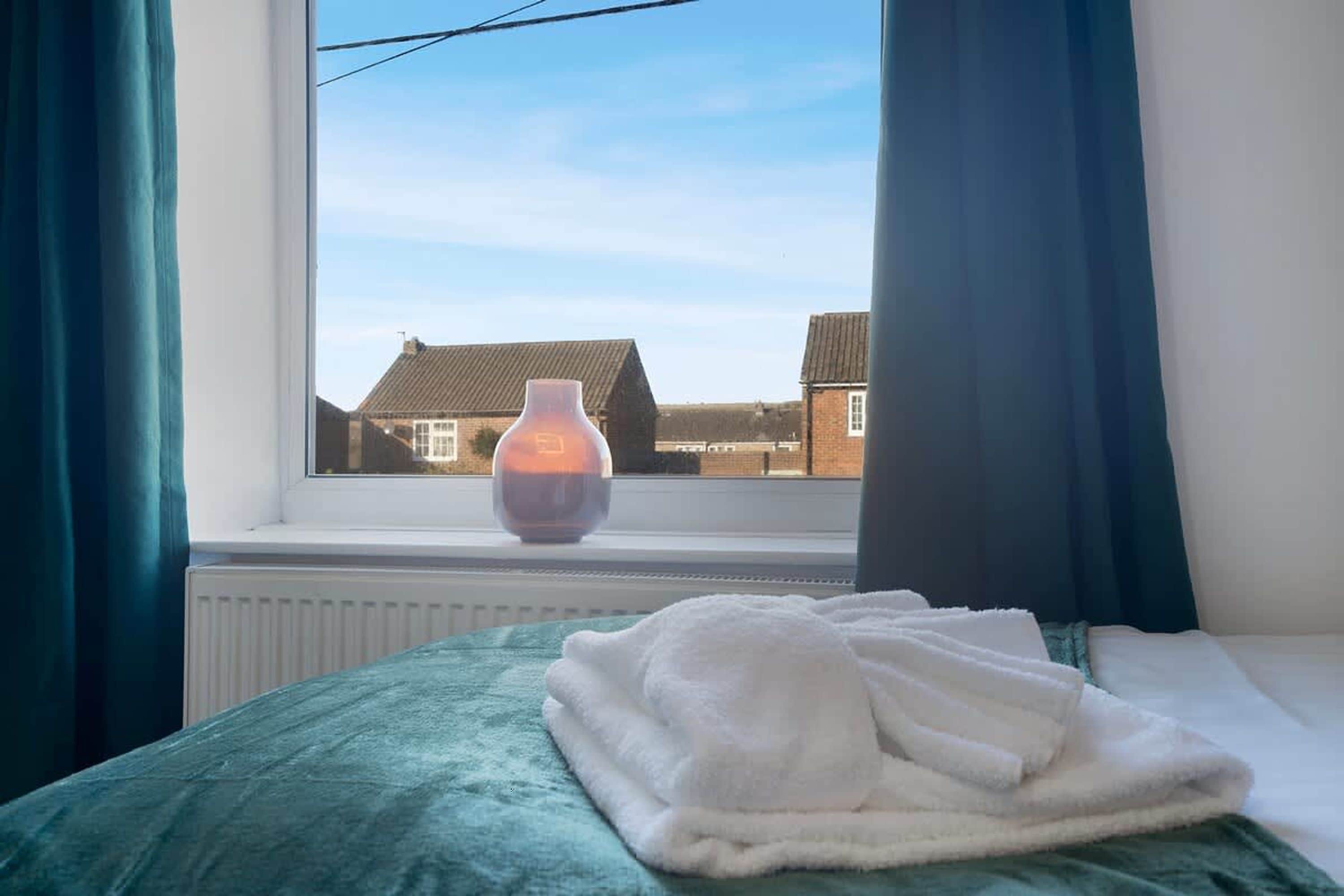 A bedroom with a bed, a window, and a vase on the windowsill.