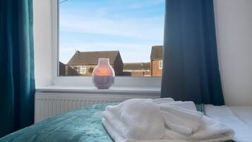 A bedroom with a bed, a window, and a vase on the windowsill.