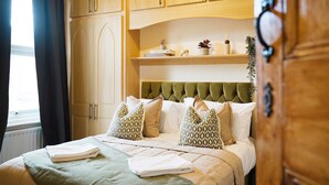 A hotel room with a bed, a window with curtains, wooden cabinets, and a shelf with decorative items. - Elegant 4BR Houghton St Sleeps 7 by Stay With Us (Hartlepool)