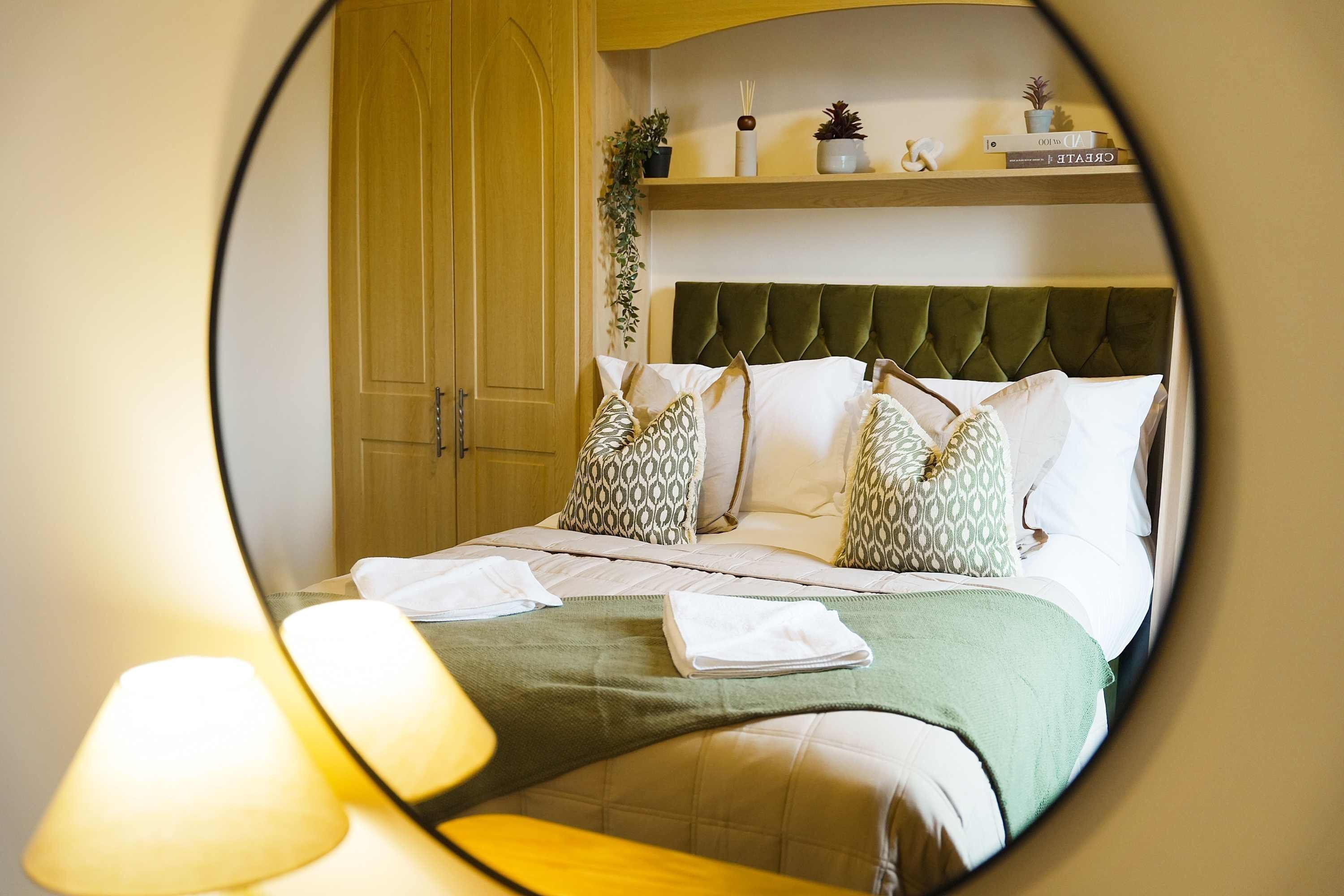 A hotel room with a bed, a green upholstered headboard, and a wooden wardrobe.
