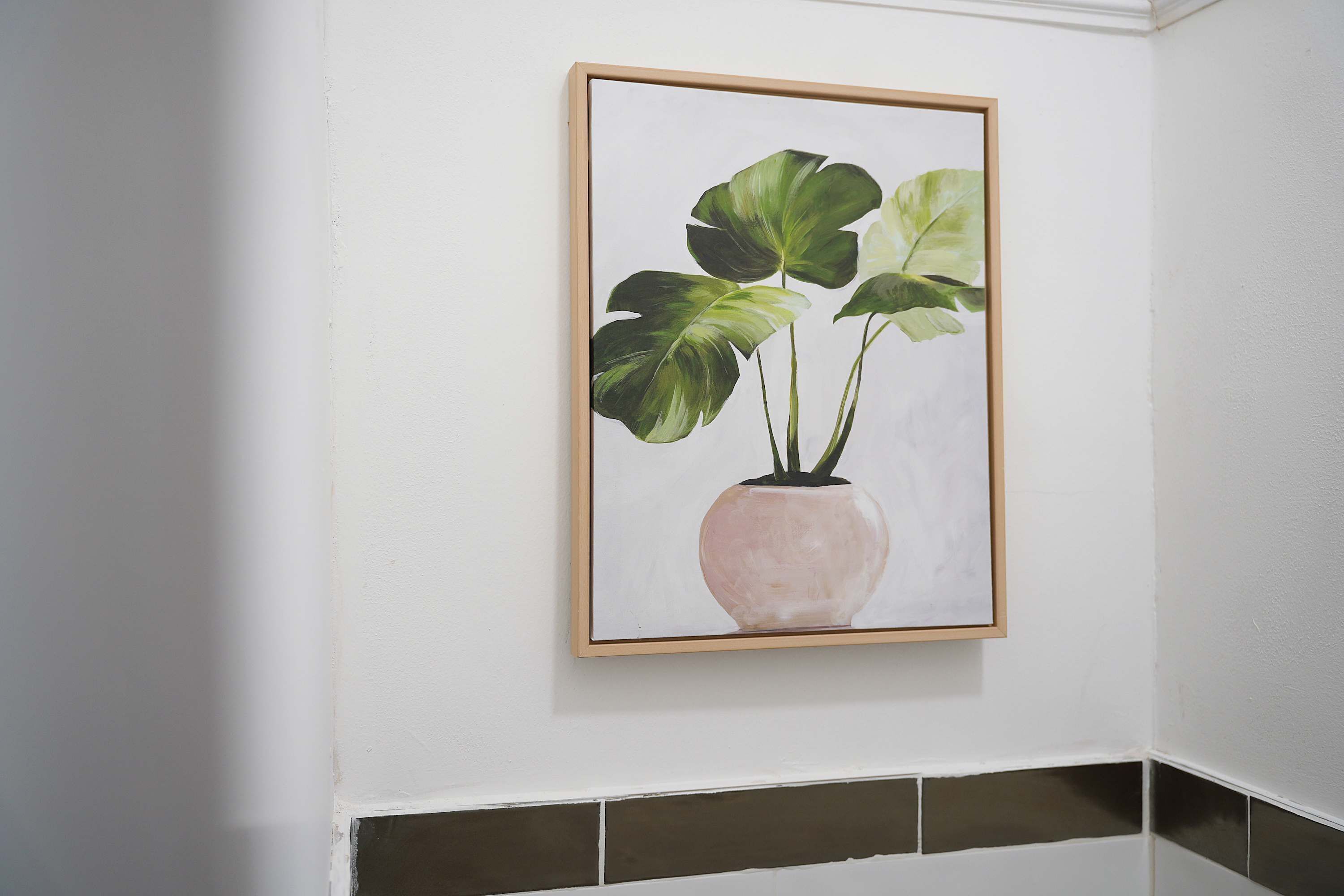 A framed painting of a plant in a vase on a white wall.