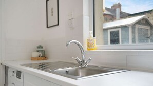 A kitchen with a stainless steel sink, a window with a view of buildings, and a bottle of hand soap on the windowsill. - Elegant 4BR Houghton St Sleeps 7 by Stay With Us (Hartlepool)
