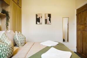 A bedroom with a bed, pillows, a bedside table, a mirror, and two abstract paintings on the wall. - Elegant 4BR Houghton St Sleeps 7 by Stay With Us (Hartlepool)