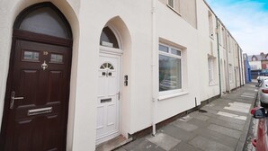 A row of terraced houses with white walls and dark brown doors, a narrow street, and parked cars. - Elegant 4BR Houghton St Sleeps 7 by Stay With Us (Hartlepool)