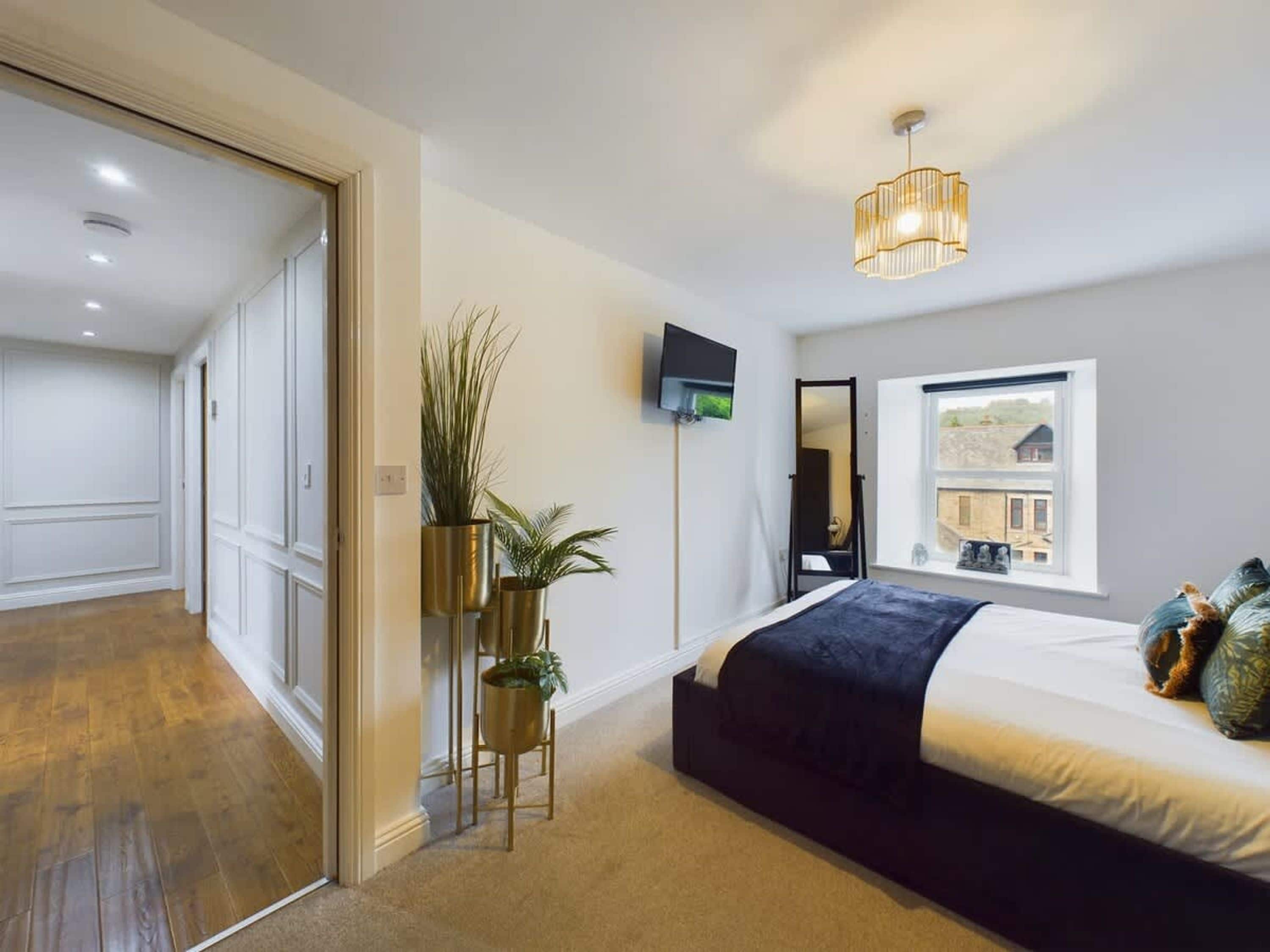 Un dormitorio con cama, televisor, ventana con vistas y una planta.