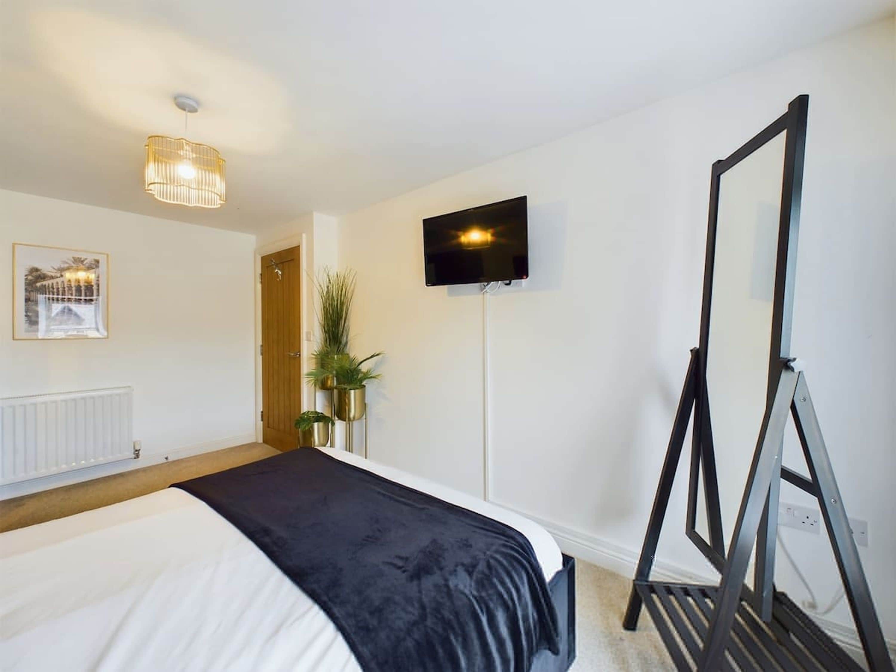 A hotel room with a bed, a television, a mirror, and a radiator.