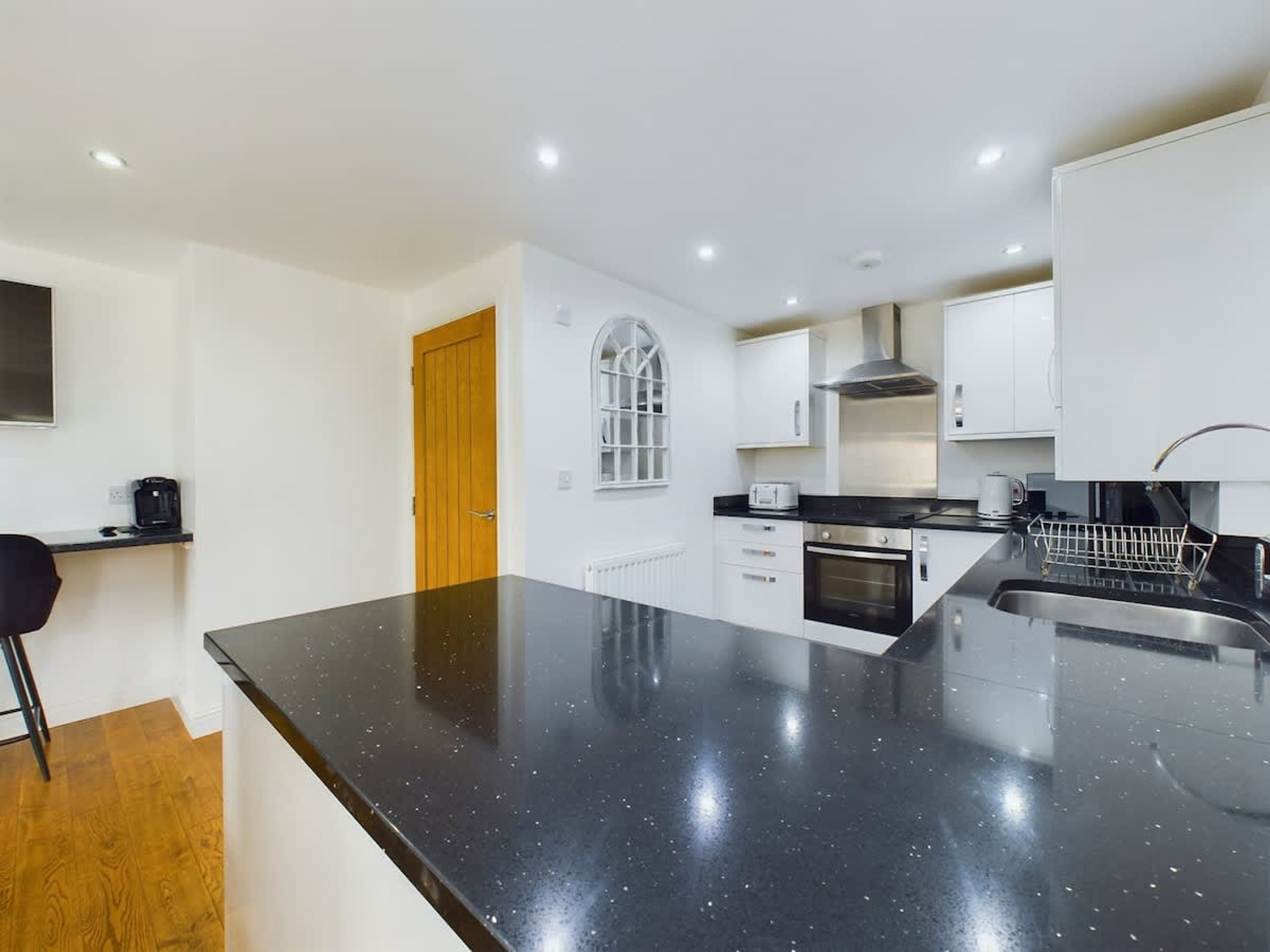 A modern kitchen with a large island, built-in oven, and white cabinetry.