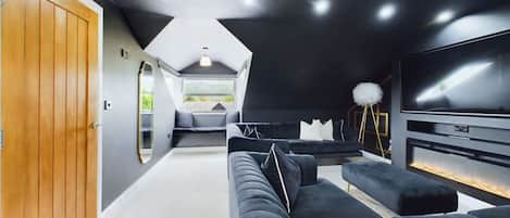 A modern living room with a large flat-screen TV, a sofa, and a ceiling with recessed lighting.