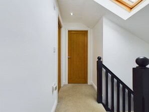 A narrow hallway with a wooden door at the end, a black railing with a spherical finial, and a skylight above. - Modern 4 Bed Walk to Pubs Shops and Countryside (Bishop Auckland)