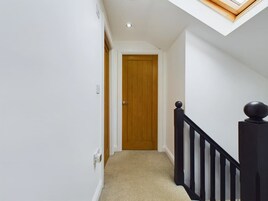 Um corredor estreito com uma porta de madeira no final, um corrimão preto com um ornamental esférico e um claraboia acima.