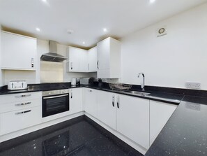 A modern kitchen with white cabinets, a black countertop, and a stainless steel range hood. - Modern 4 Bed Walk to Pubs Shops and Countryside (Bishop Auckland)