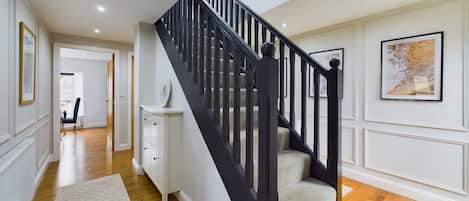A staircase with black railings leading to a second floor, a white wall with a framed picture, and a wooden floor.