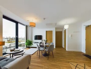 Ein modernes Wohnzimmer mit Essbereich, großen Fenstern und einem Flachbildfernseher.