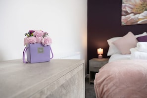 A room with a bed, a nightstand with a candle, and a purple bag with flowers on a wooden nightstand. - 3 Bed in Sunderland With Free Wifi (Sunderland)