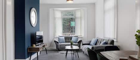 A modern living room with a grey sofa, a coffee table, and a TV on a stand.