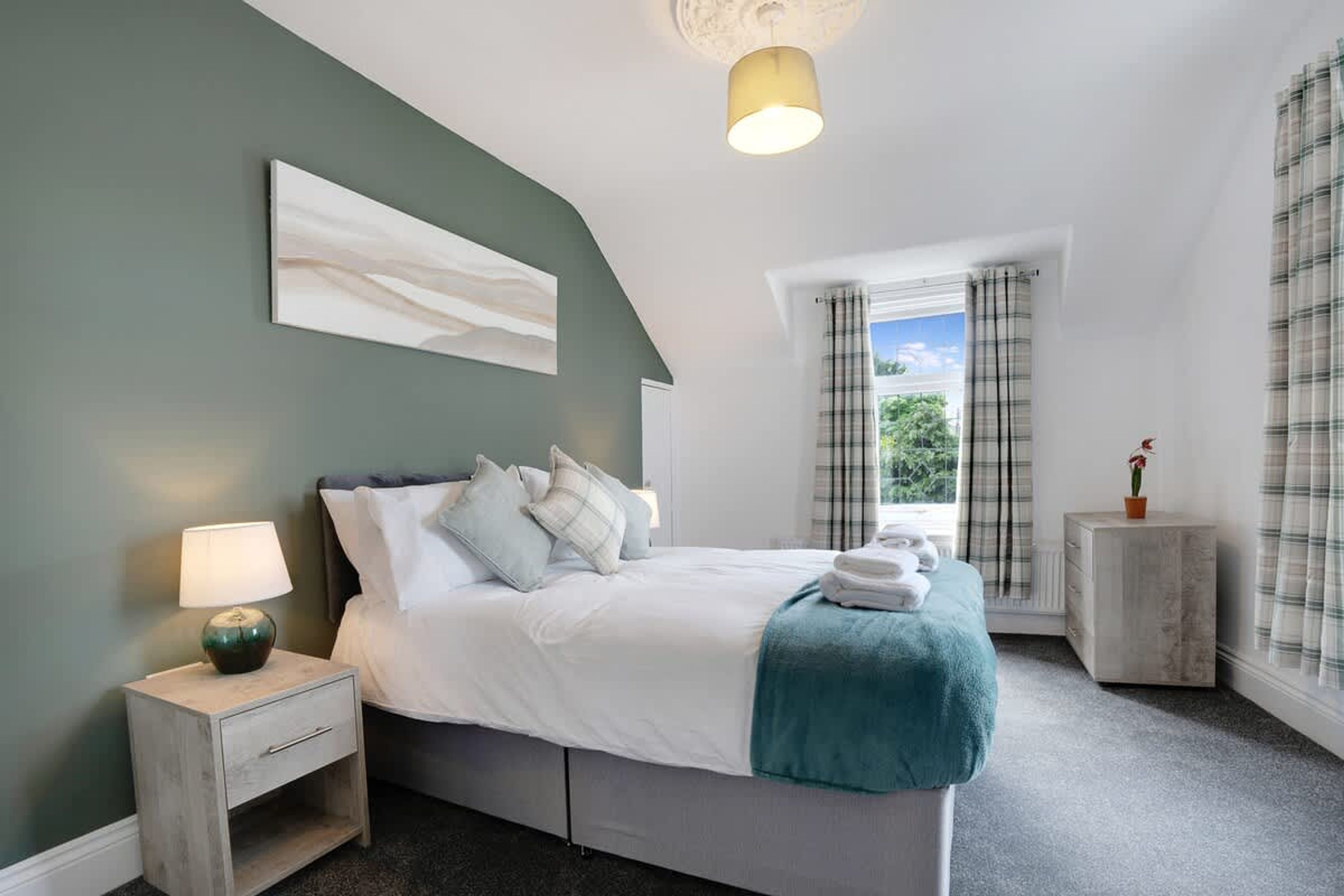 A bedroom with a bed, bedside table, lamp, and a window with curtains.