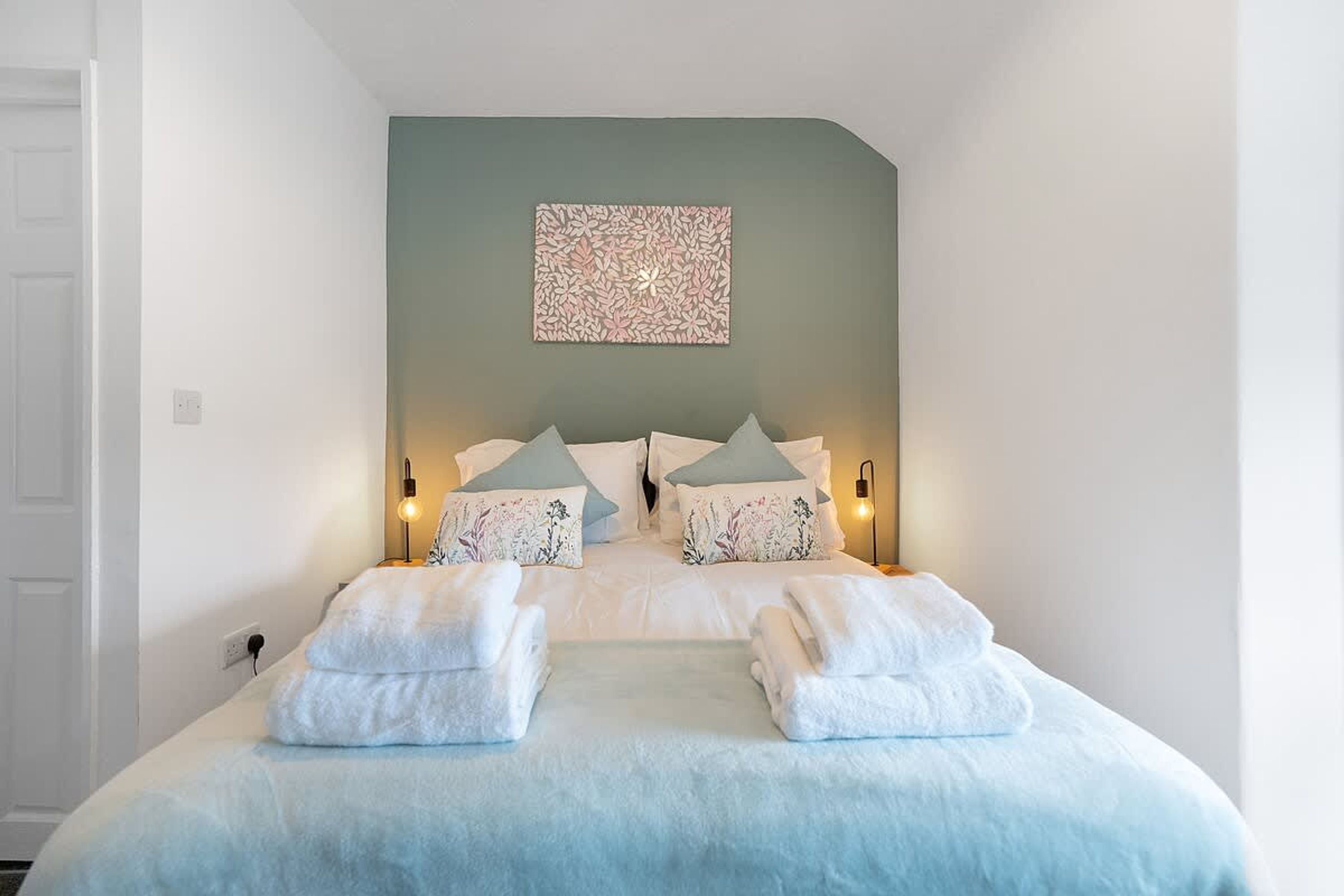 A bedroom with a bed, pillows, a wall-mounted artwork, and bedside lamps.