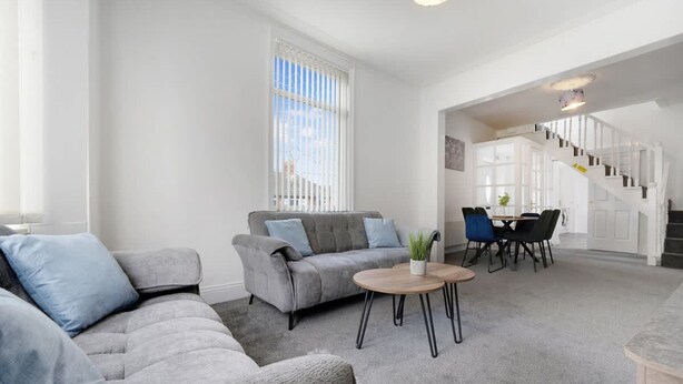 A modern living room with a grey sofa, a coffee table, and a dining area with chairs and a table. - 3 Bed in Sunderland With Free Wifi (Sunderland)