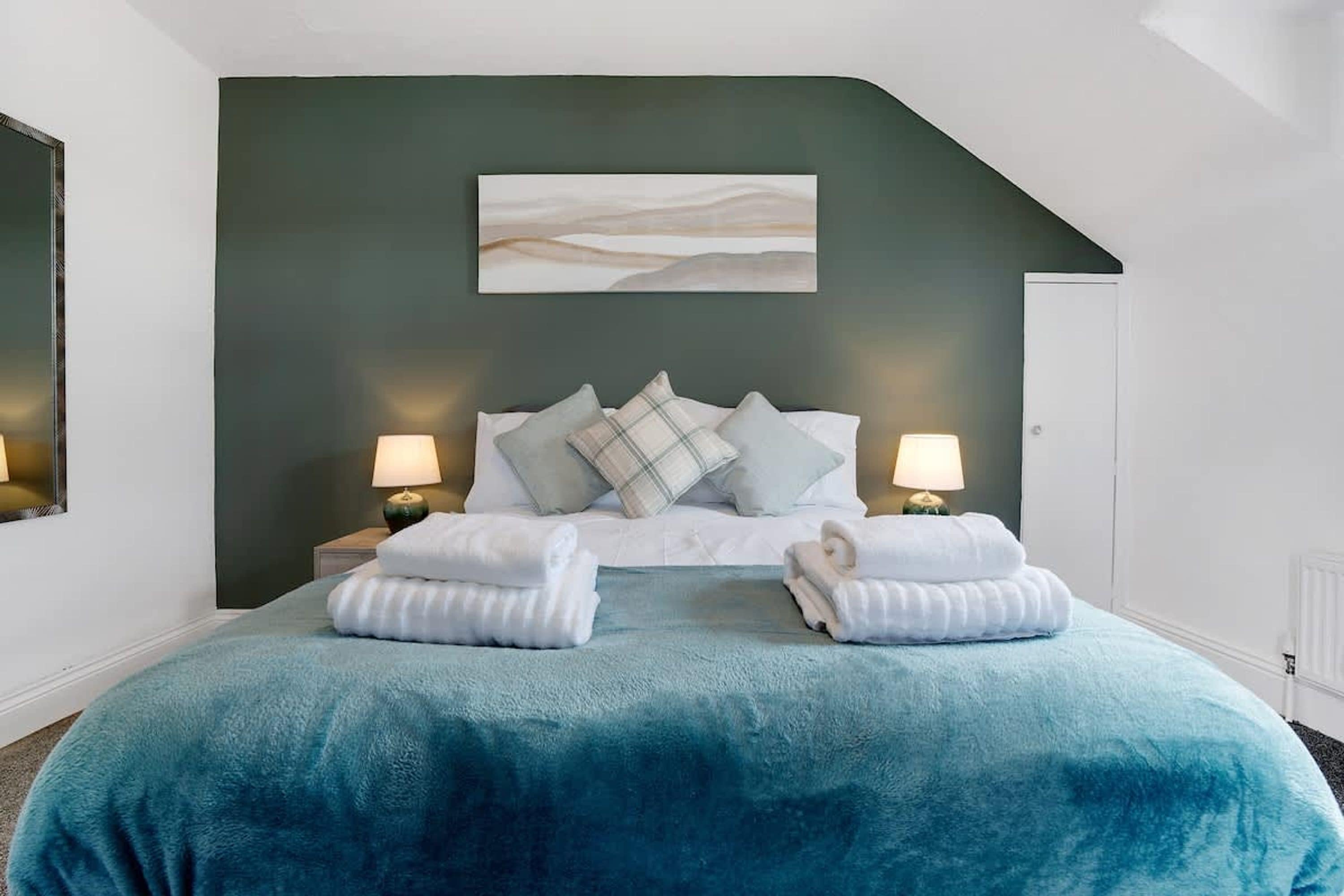 A bedroom with a bed, pillows, a nightstand, a lamp, and a painting on the wall.