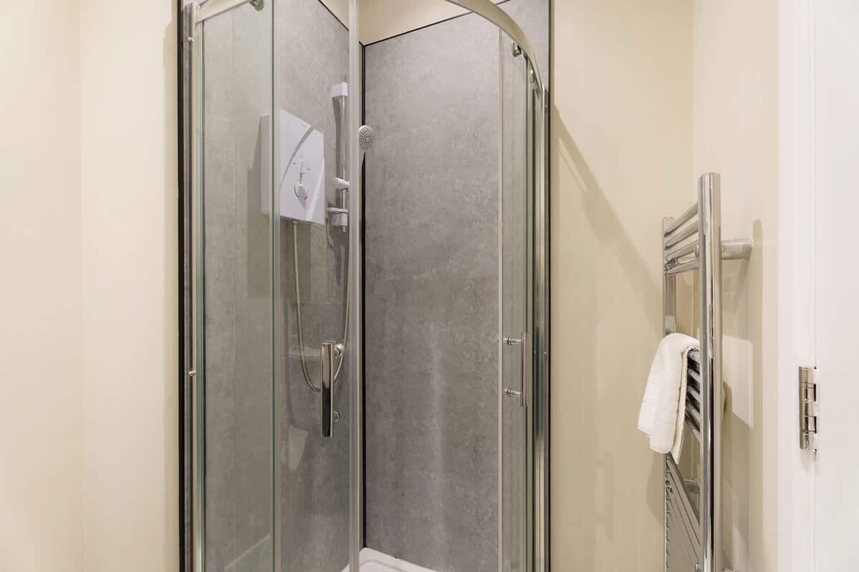 Eine begehbare Dusche mit Glaswänden, einer Handbrause und einem Handtuchhalter mit Handtuch.