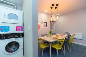 A compact living space with a washing machine, a dining area with yellow chairs, and a hanging light fixture. - Luxurious 1 Bedroom With Private Parking and Wifi (Middlesbrough)