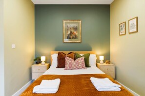 A hotel room with a large bed, two nightstands, a wall-mounted painting, and two framed pictures. - Luxurious 1 Bedroom With Private Parking and Wifi (Middlesbrough)
