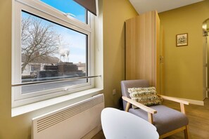 A room with a window, a radiator, a chair with a cushion, a wooden wardrobe, and a framed picture on the wall. - Luxurious 1 Bedroom With Private Parking and Wifi (Middlesbrough)