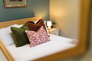 A neatly made bed with white sheets, a green pillow, and a pink and brown patterned pillow. - Luxurious 1 Bedroom With Private Parking and Wifi (Middlesbrough)