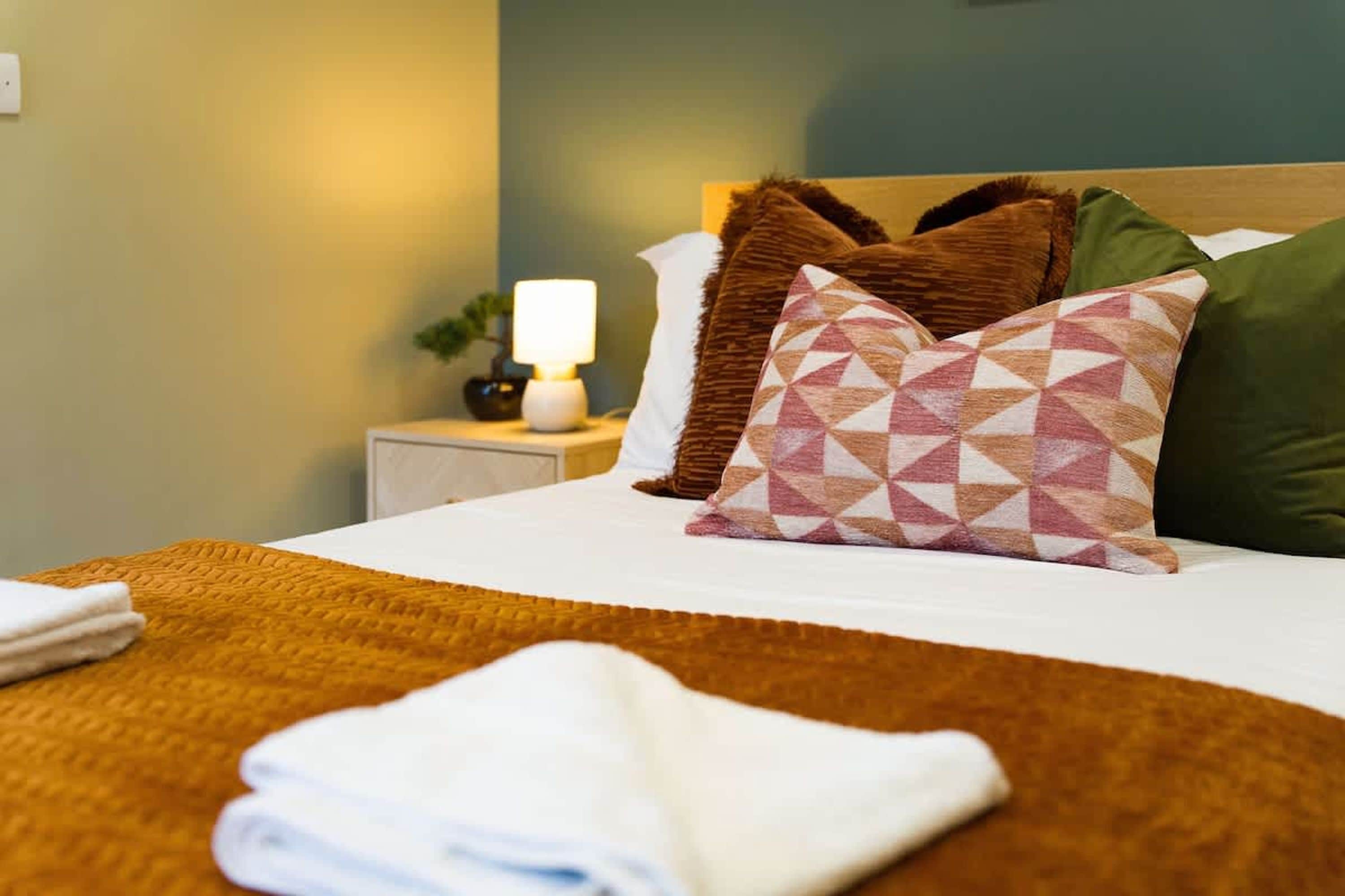 A neatly made bed with a white duvet, a brown throw blanket, and patterned pillows.