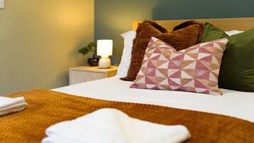 A neatly made bed with a white duvet, a brown throw blanket, and patterned pillows.