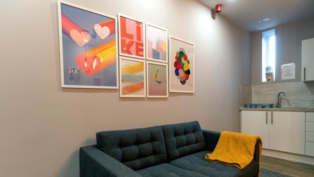 Ein Wohnzimmer mit einem dunkelblauen Sofa, einer gelben Decke und vier gerahmten Kunstwerken an der Wand.