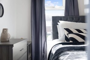 A bedroom with a bed, a bedside table, a dresser, and a window with curtains. - Stylish Home Near Durham Heritage Coast Sleeps 5 (Durham)