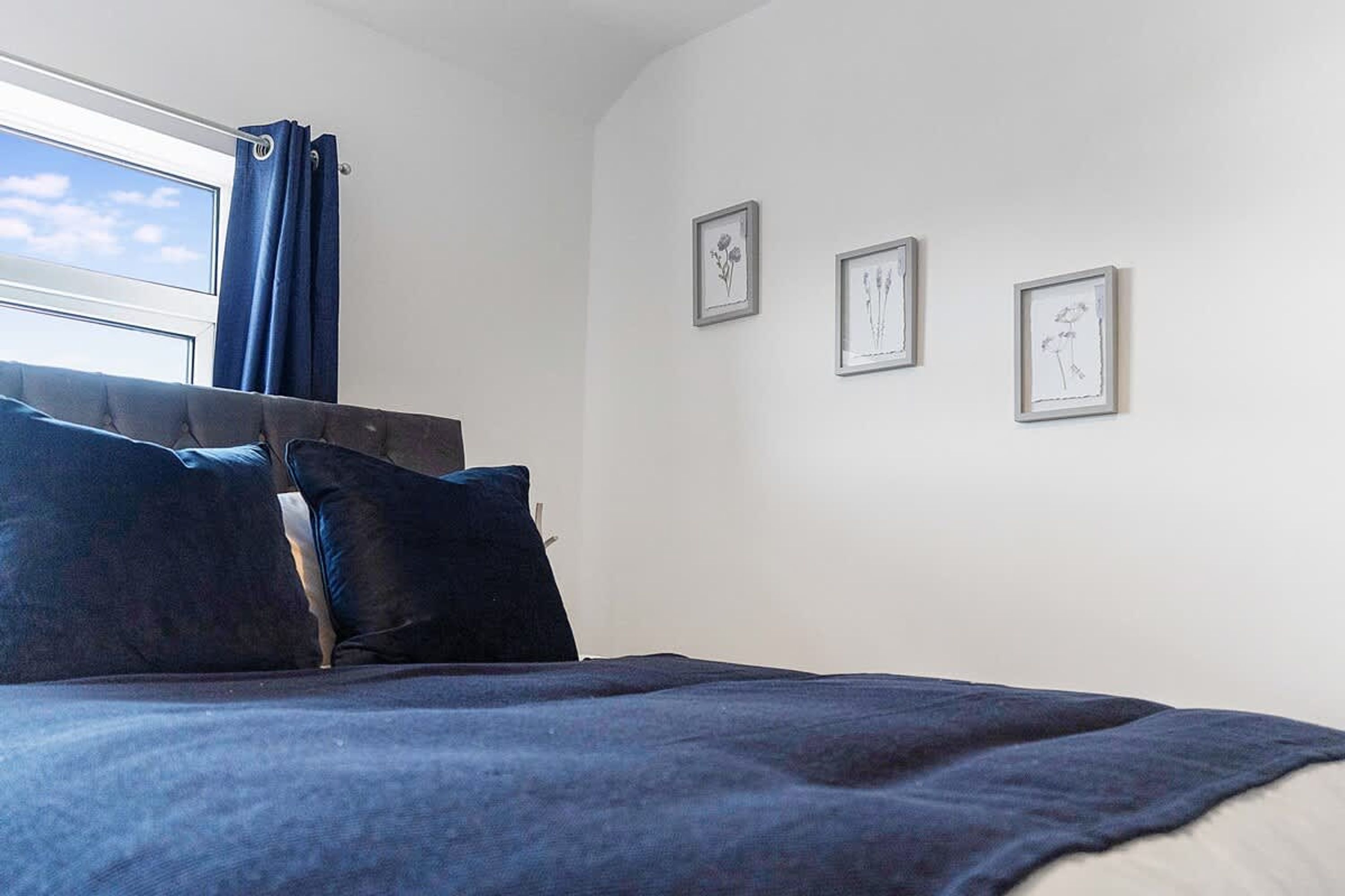 A bedroom with a bed, a window with curtains, and three framed pictures on the wall.