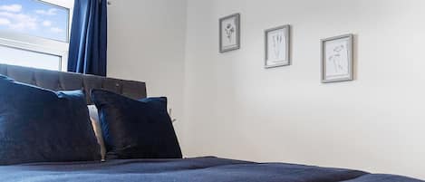 A bedroom with a bed, a window with curtains, and three framed pictures on the wall.